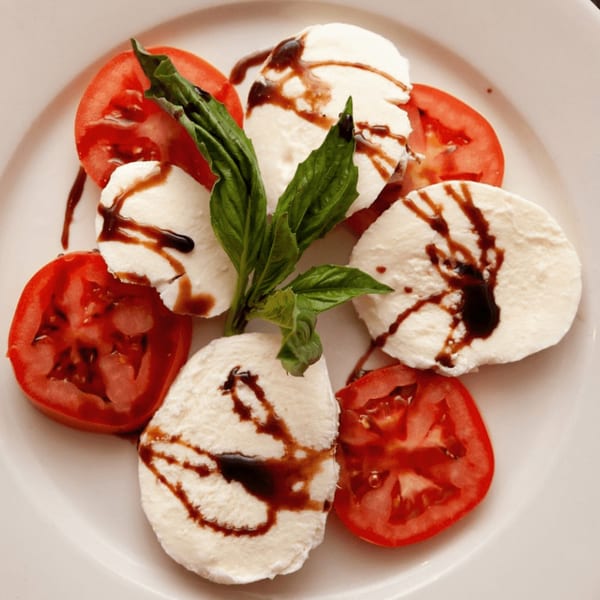 Caprese salad with sliced tomatoes, mozzarella, fresh basil, and balsamic glaze on a white plate.