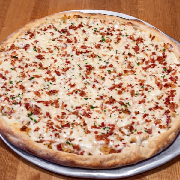 A whole Sayville Pizza white pizza with melted cheese, bacon bits, and parsley on a metal tray.