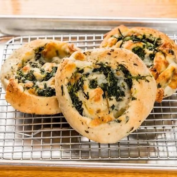 Three golden-brown Sayville Pizza spinach pinwheels with melted cheese on a metal cooling rack.