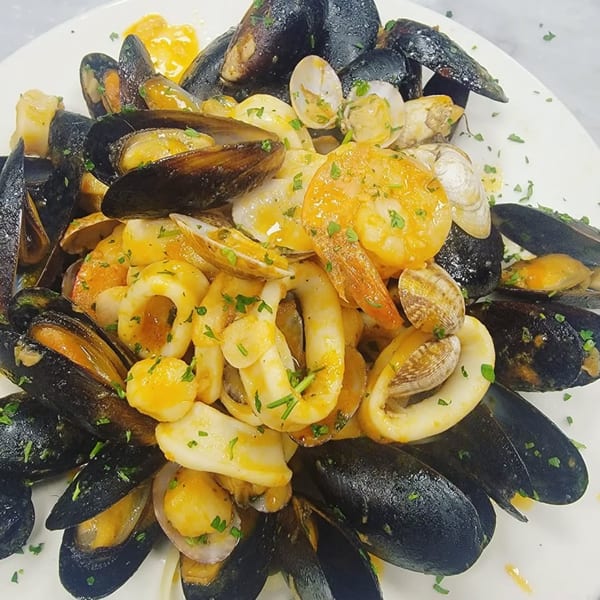 A close-up of a seafood dish with mussels, clams, shrimp, and calamari in a yellow sauce.