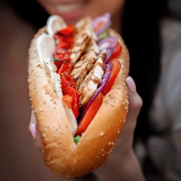 A person holding a grilled chicken sub sandwich filled with tomatoes, onions, and sauce.
