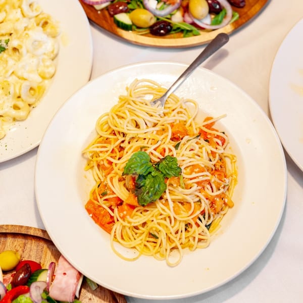 Spaghetti with tomato sauce and fresh basil, with other Italian dishes in the background.