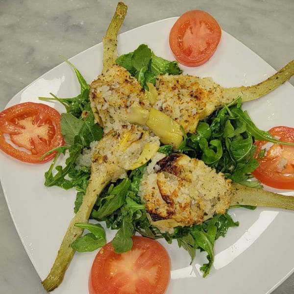 Baked artichoke hearts with breadcrumbs, served on a bed of arugula with tomato slices.